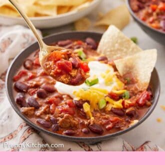 Pinterest graphic of a spoonful of turkey chili lifted out of the bowl with a bowl of chips in the background.