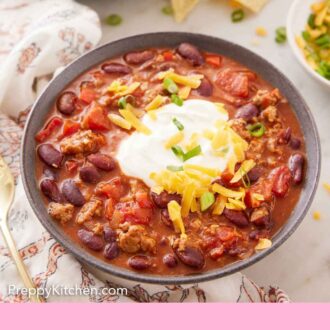 Pinterest graphic of a bowl of turkey chili with a dollop of sour cream on top with shredded cheese and green onions.