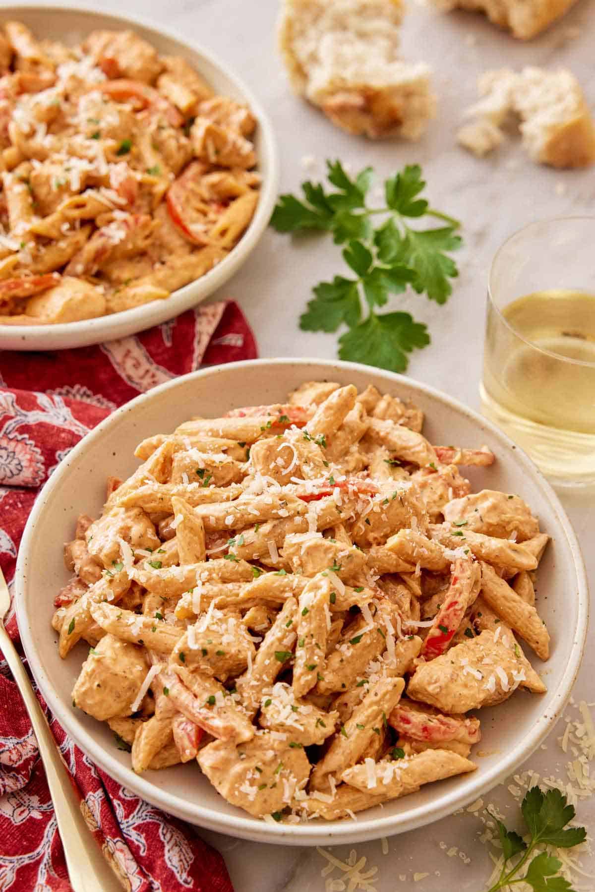 A plate of Cajun chicken pasta with a glass of wine, torn bread, and more pasta in the back.