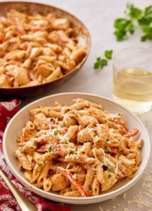 A plate of Cajun chicken pasta with a glass of wine and skillet in the background.