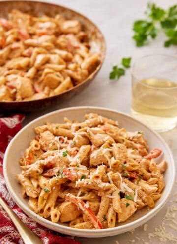 A plate of Cajun chicken pasta with a glass of wine and skillet in the background.