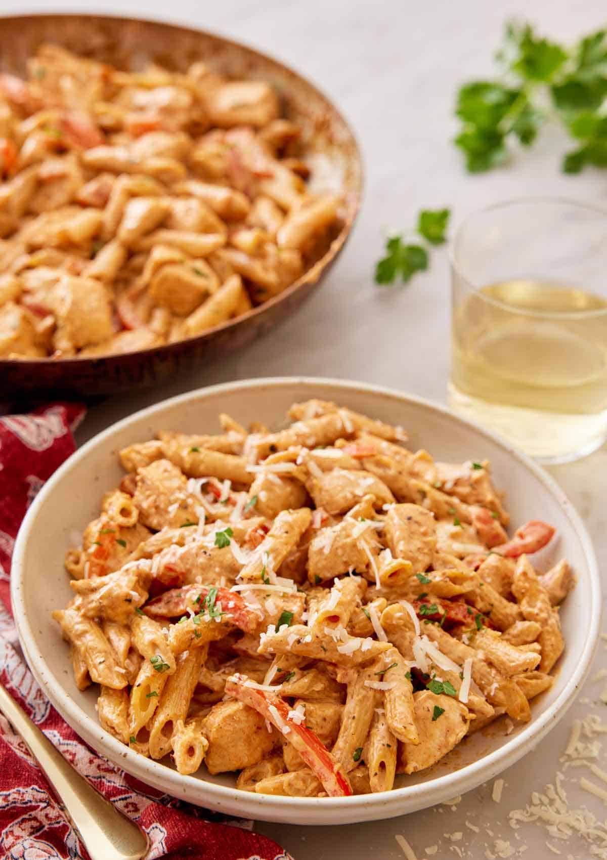 A plate of Cajun chicken pasta with a glass of wine and skillet in the background.