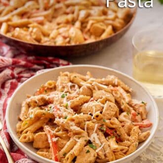Pinterest graphic of a plate of Cajun chicken pasta with a glass of wine and a skillet of pasta in the background.