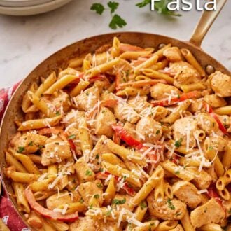 Pinterest graphic of a skillet of Cajun chicken pasta with shredded parmesan on top with parsley in the background.