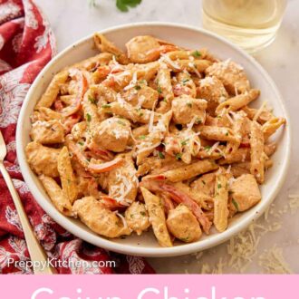 Pinterest graphic of a plate of Cajun chicken pasta with a glass of wine, parsley, and shredded parmesan on the counter.