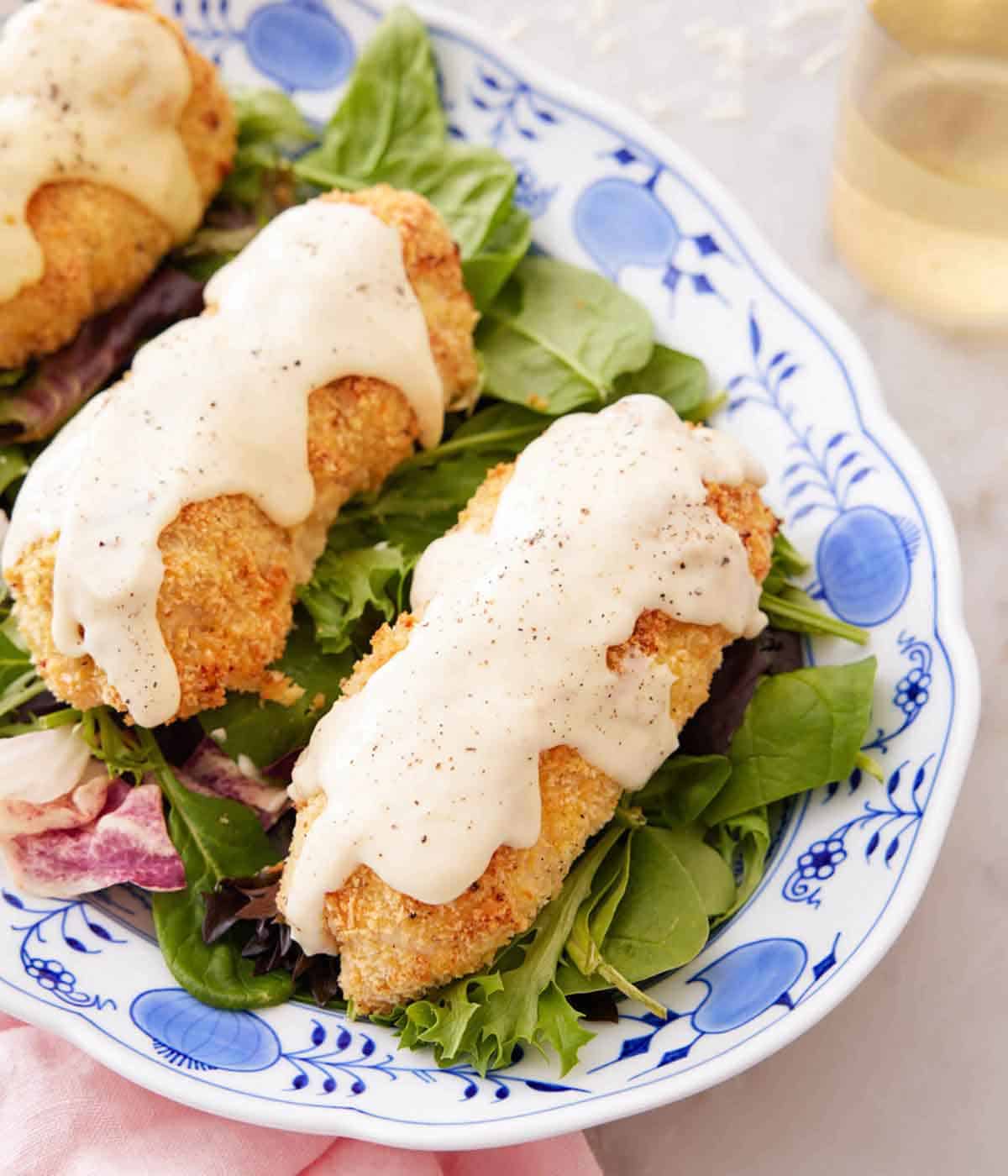 Overhead view of a platter with chicken cordon bleu with sauce on top, over salad.