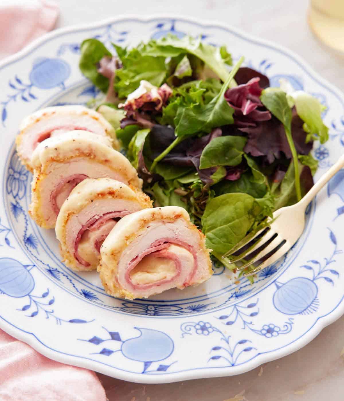 A plate with a chicken cordon bleu sliced with a side of salad with a fork.