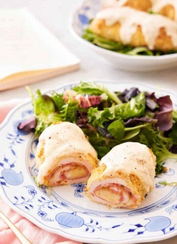 A plate with a serving of chicken cordon bleu cut in half, showing the middle filling with a salad in the back.