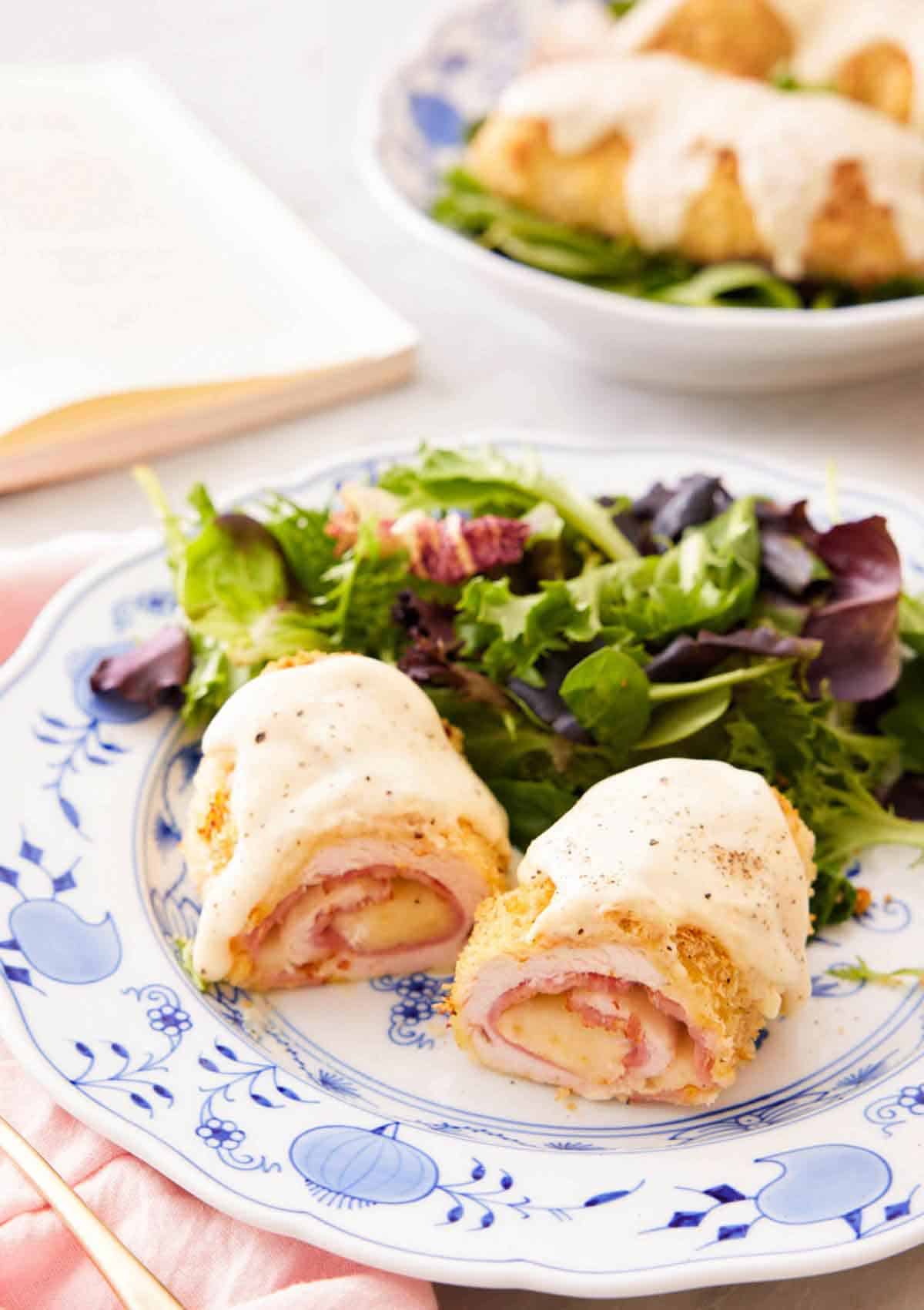 A plate with a serving of chicken cordon bleu cut in half, showing the middle filling with a salad in the back.