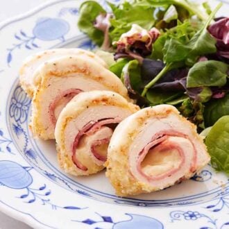A plate with chicken cordon bleu cut into four pieces with a side of salad.