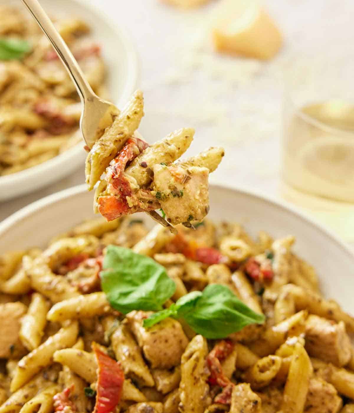 A forkful of chicken pesto pasta lifted up from the plate.