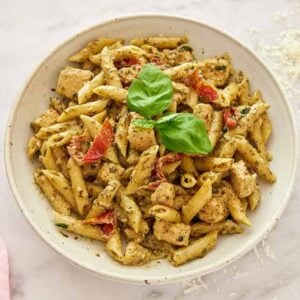 Overhead view of a plate of chicken pesto pasta with fresh basil on top with a block of parmesan shredded on the side.