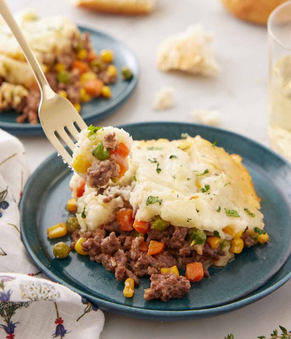 A forkful of shepherd's pie lifted from a plate, showing the mashed potatoes, meat, and vegetables.