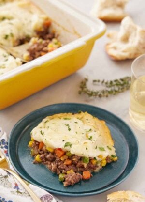A plate with a serving of shepherd's pie with a baking dish in the back.