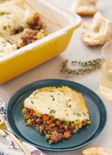 A plate with a serving of shepherd's pie with a baking dish in the back.