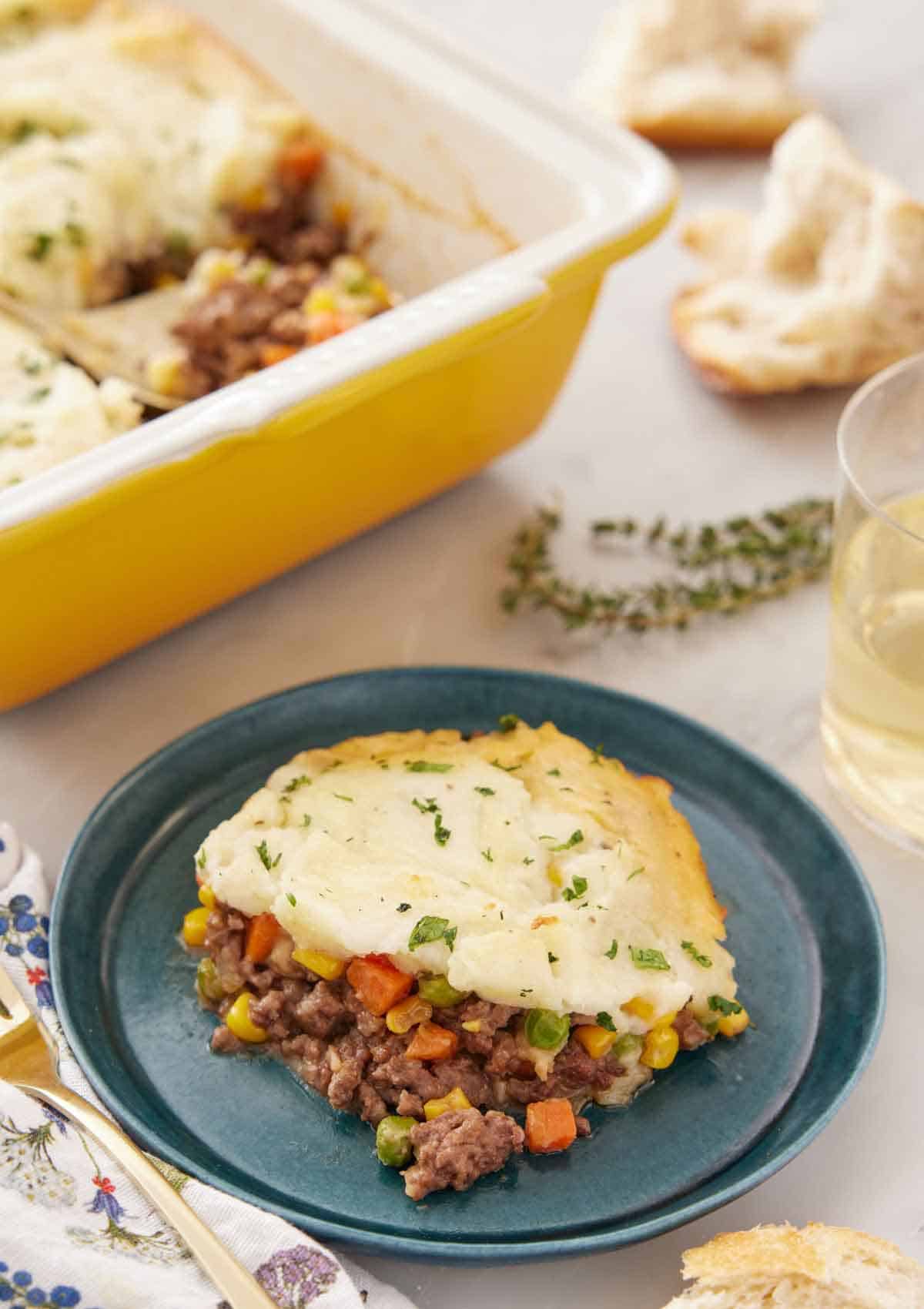 A plate with a serving of shepherd's pie with a baking dish in the back.