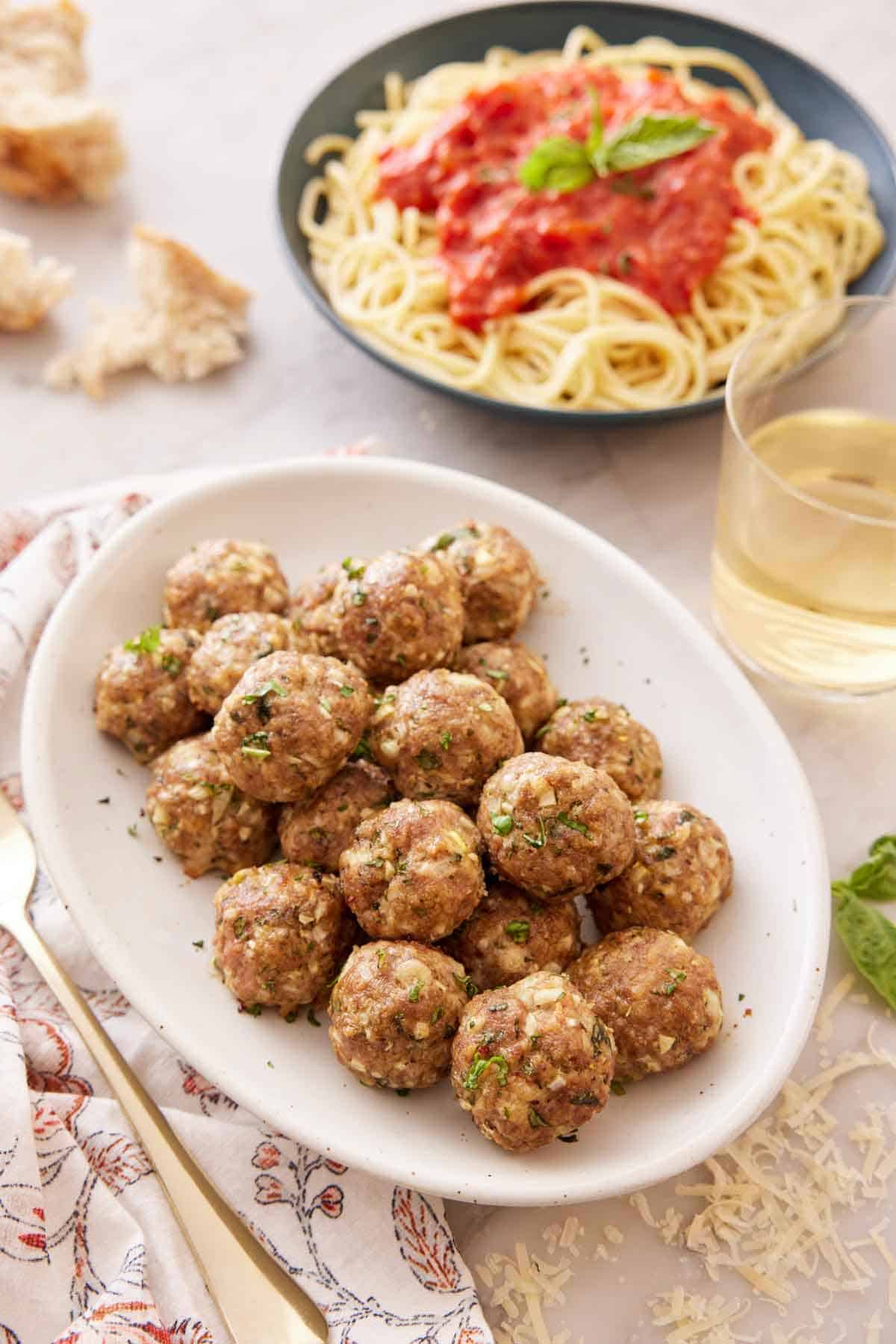 A platter of turkey meatballs with a glass of wine and a plate of noodles with sauce in the background.
