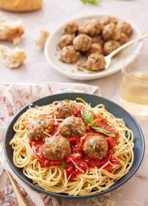 A plate of noodles with tomato sauce topped with turkey meatballs and basil with a platter of meatballs in the background.