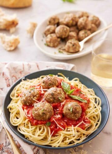 A plate of noodles with tomato sauce topped with turkey meatballs and basil with a platter of meatballs in the background.