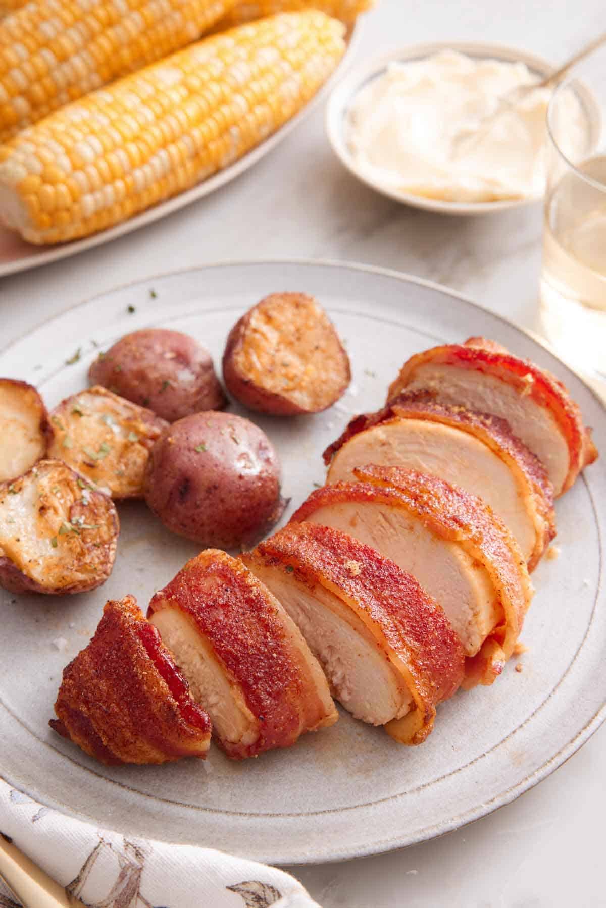 A plate with a serving of bacon wrapped chicken sliced into bite-sized pieces with a side of baby potatoes.