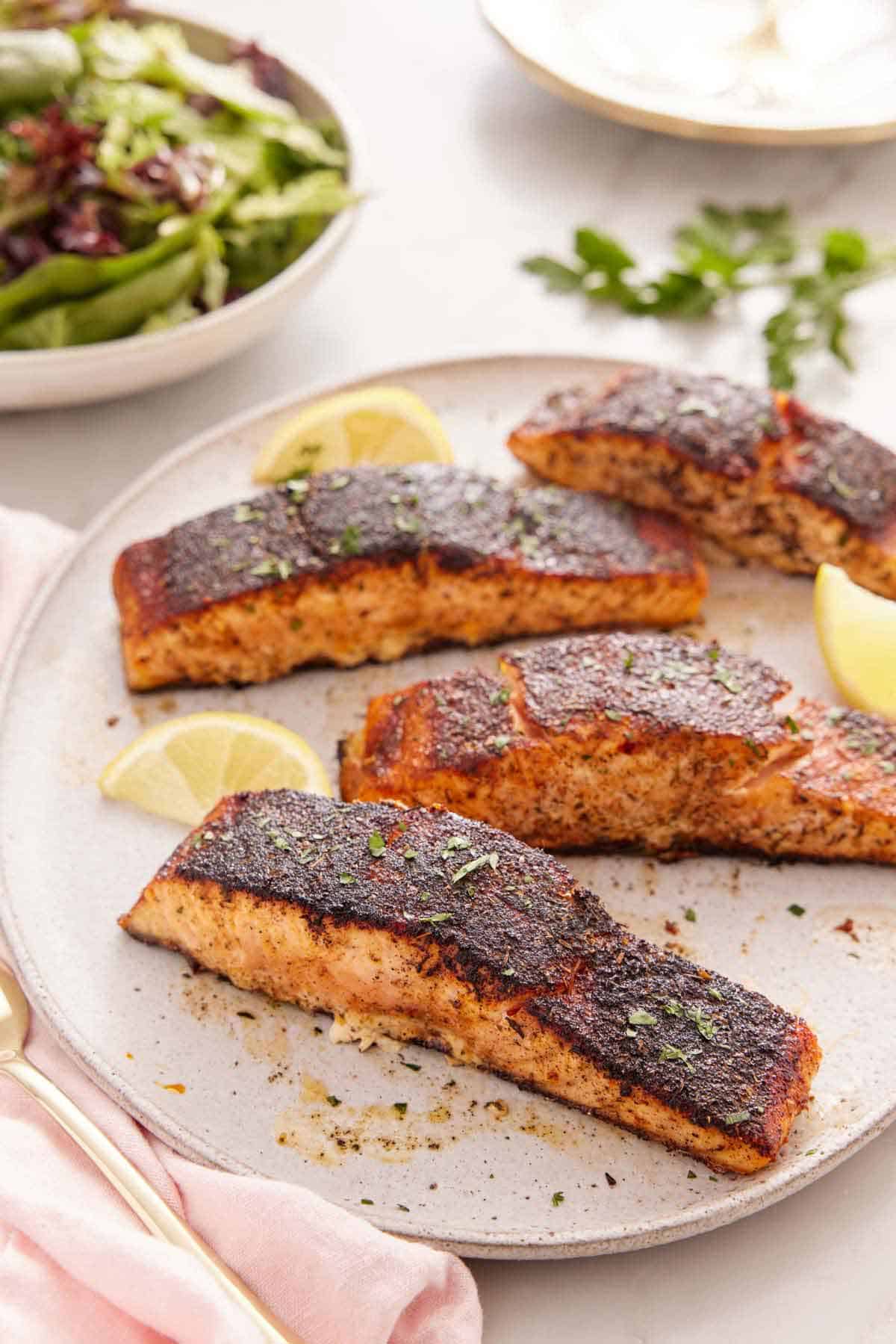 A platter with four pieces of blackened salmon with lemon wedges.