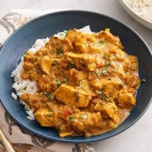 A bowl of rice with chicken curry on top with some more rice on the side and a fork.
