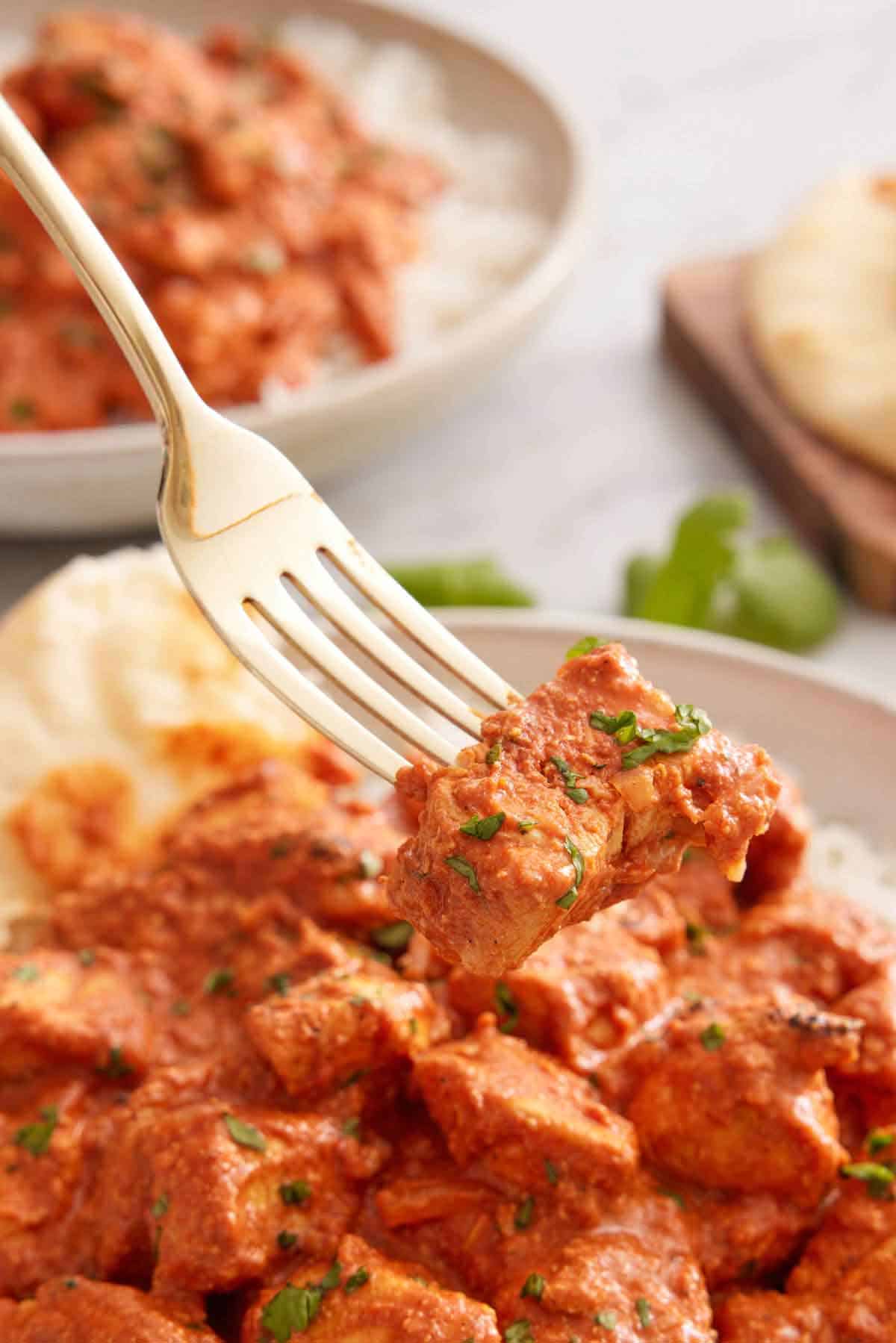 A spoonful of chicken tikka masala with cilantro lifted from a bowl.