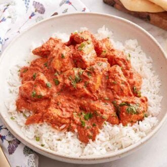 A bowl of rice with chicken tikka masala on top with a glass of wine in the back.