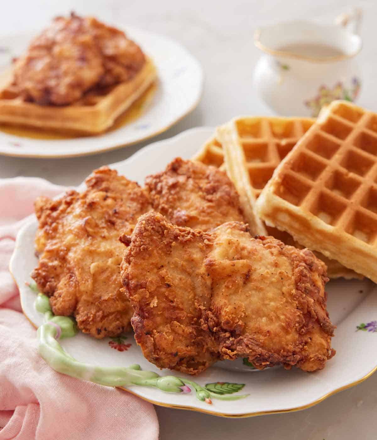 A platter with a pile of waffles on the back half and fried chicken in the front.