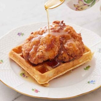 A plate with chicken and waffles with syrup poured over top.