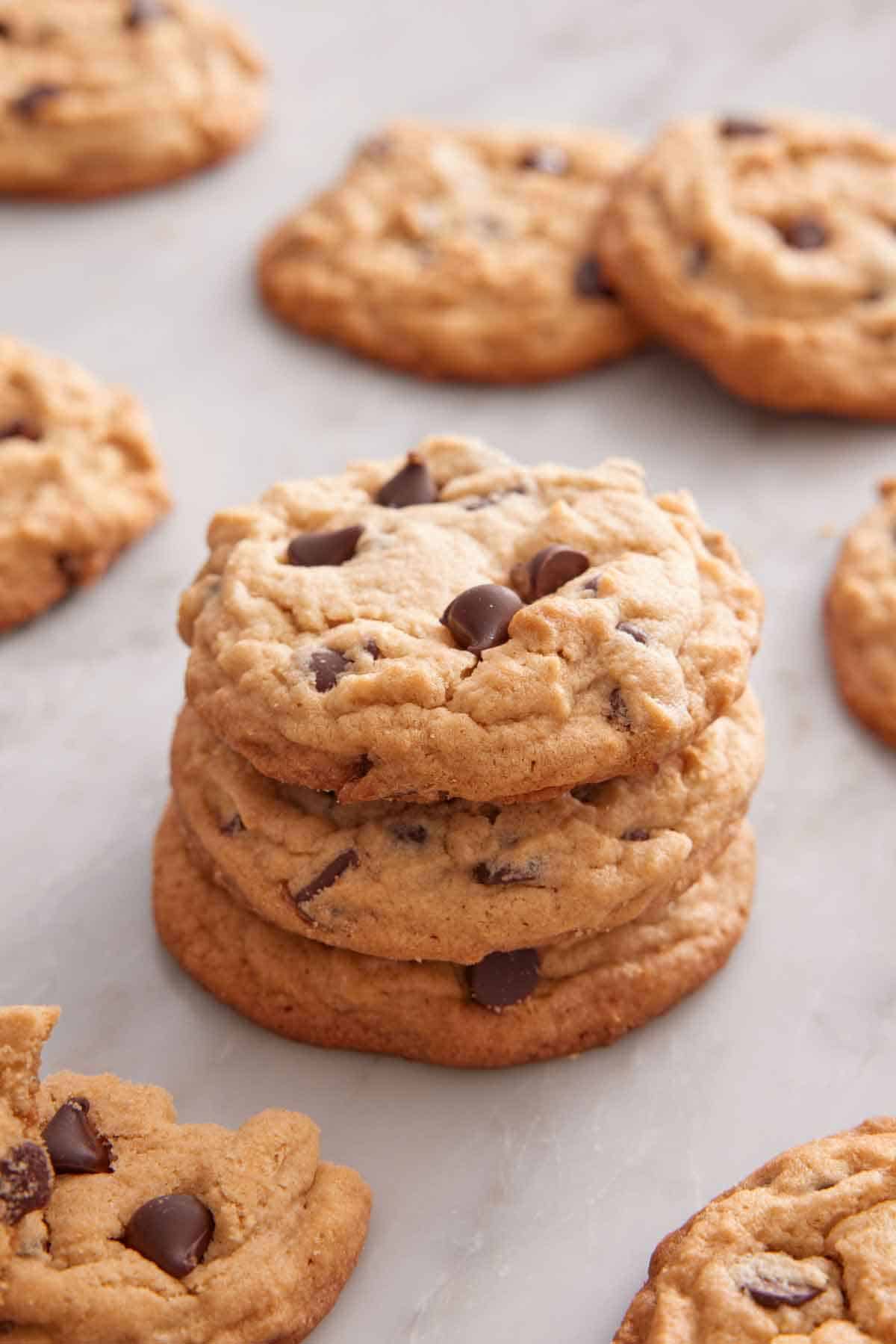 A stack of three peanut butter chocolate chip cookies with more scattered around.