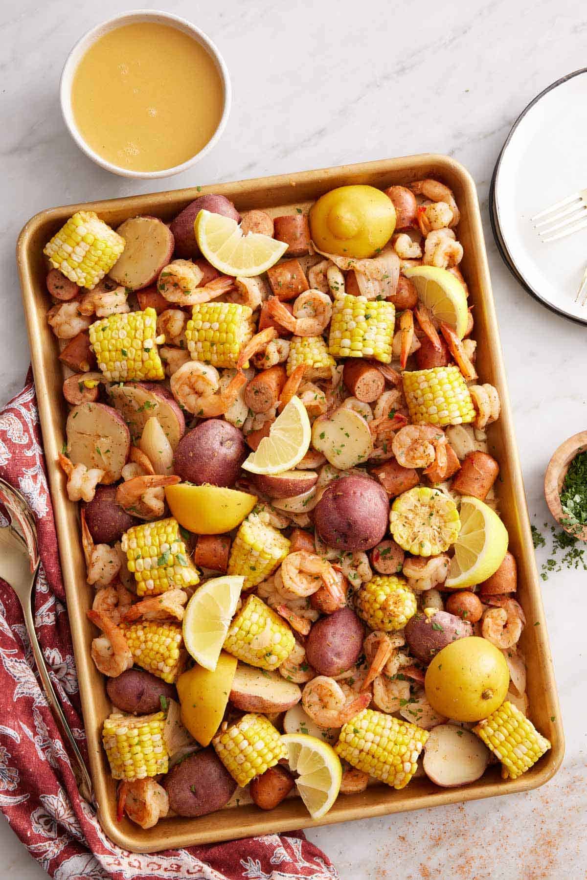 Overhead view of a sheet pan of shrimp boil with a bowl of melted butter off to the side.