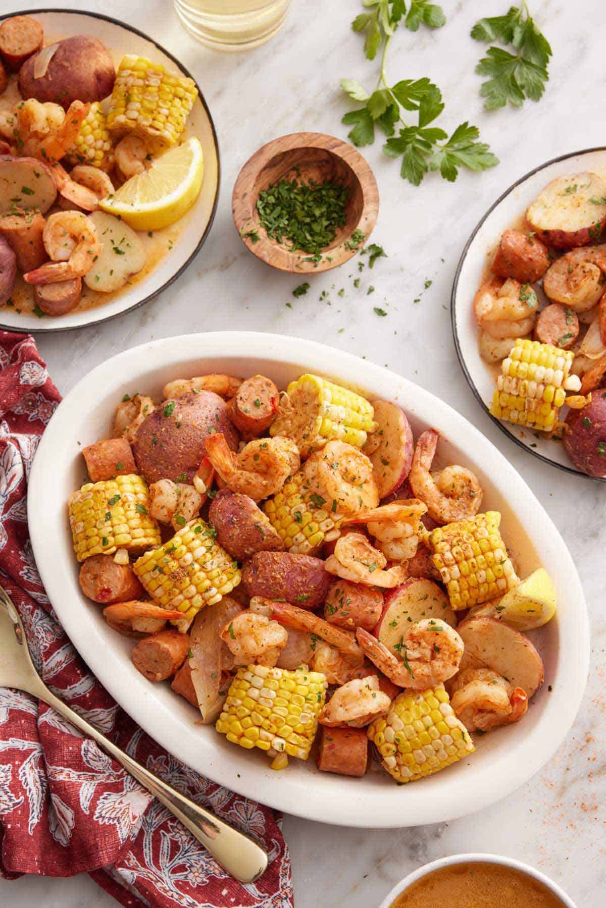 A platter of shrimp boil with plated servings and chopped parsley on the side.