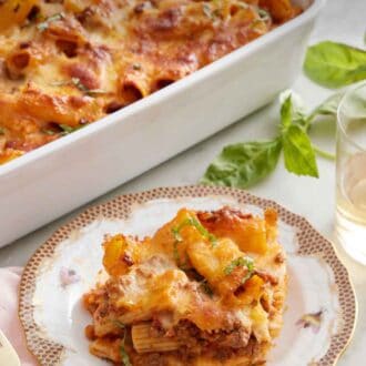 Pinterest graphic of a plate of baked rigatoni with a glass of wine, basil, and baking dish in the background.