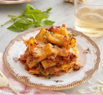 Pinterest graphic of a plate of baked rigatoni with some wine, basil, bread, and a second plate of pasta in the background.