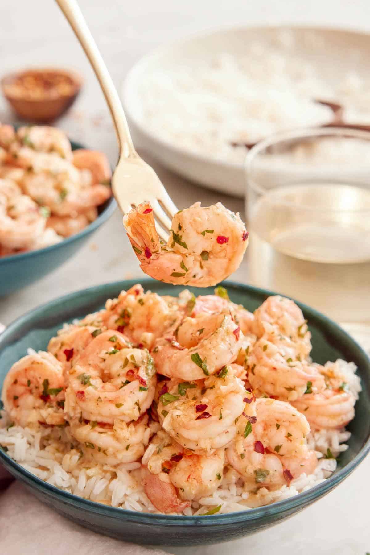 A bowl of rice with garlic shrimp on top with a fork lifting up one shrimp.