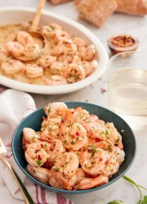 A bowl of garlic shrimp with a platter of shrimp in the back along with some wine.