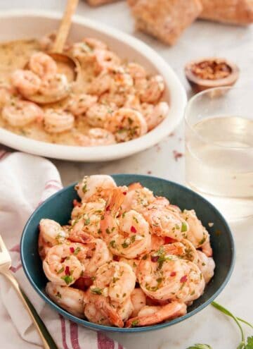 A bowl of garlic shrimp with a platter of shrimp in the back along with some wine.