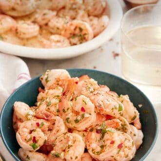 Pinterest graphic of a blue bowl of garlic shrimp with a platter of shrimp and glass of wine in the background.