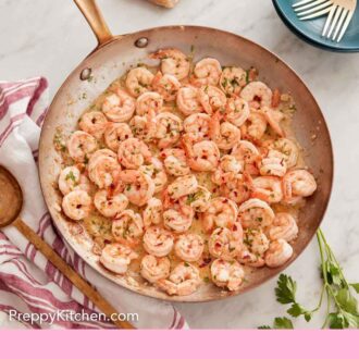 Pinterest graphic of an overhead view of a skillet of garlic shrimp with some torn bread and utensils on the side.