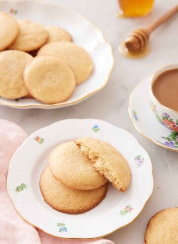 A plate with two and a half honey cookies with a platter of more cookies and cup of coffee in the back.