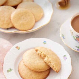 Pinterest graphic of a plate with two and a half honey cookies with a platter of more cookies behind it.