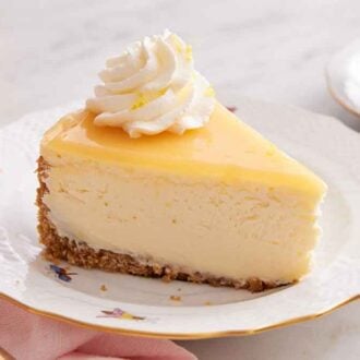 A slice of lemon cheesecake with a dollop of whipped cream topped with lemon zest.