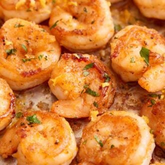Close up view of sautéed shrimp in a single layer with lemon zest and parsley.