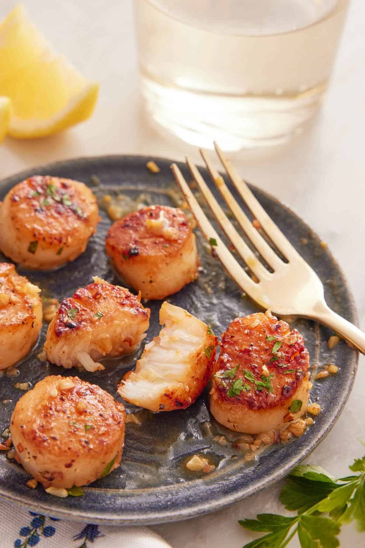 A plate with a serving of seared scallops with one cut in half and a fork on the plate.