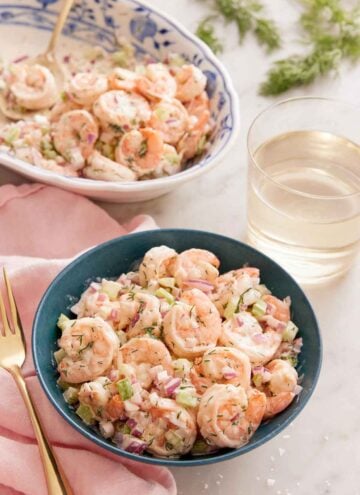 A bowl of shrimp salad with a glass of wine and platter of more shrimp in the background.