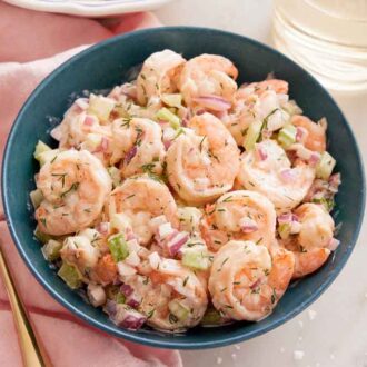 Overhead view of a bowl of shrimp salad with a fork and glass of wine beside it.