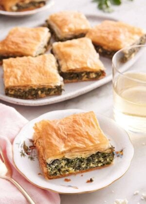 A plate with a square piece of spanakopita with a platter with more in the background.