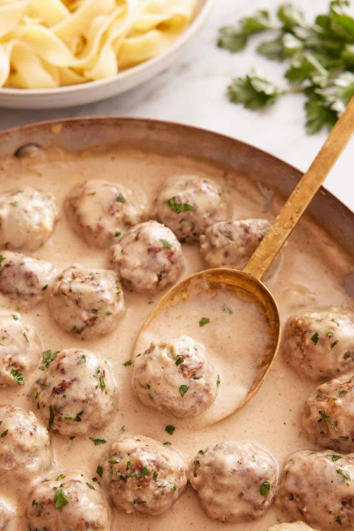 A skillet of Swedish meatballs with a serving spoon tucked underneath one meatball.