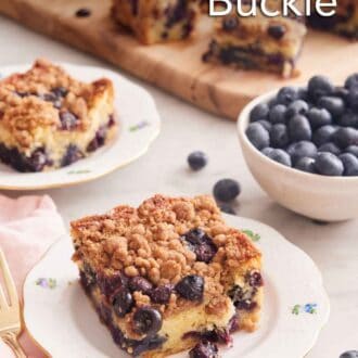 Pinterest graphic of a plate with a piece of blueberry buckle with a bowl of blueberries and additional cut pieces in the background.
